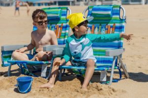 little boys playing on the beach two boys sitting on a beach chair on the sand